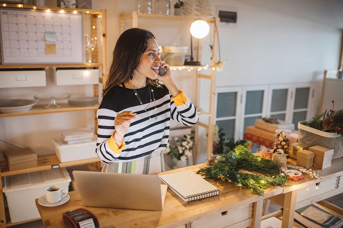Working woman at gift shop using mobile phone to receive new order from customer