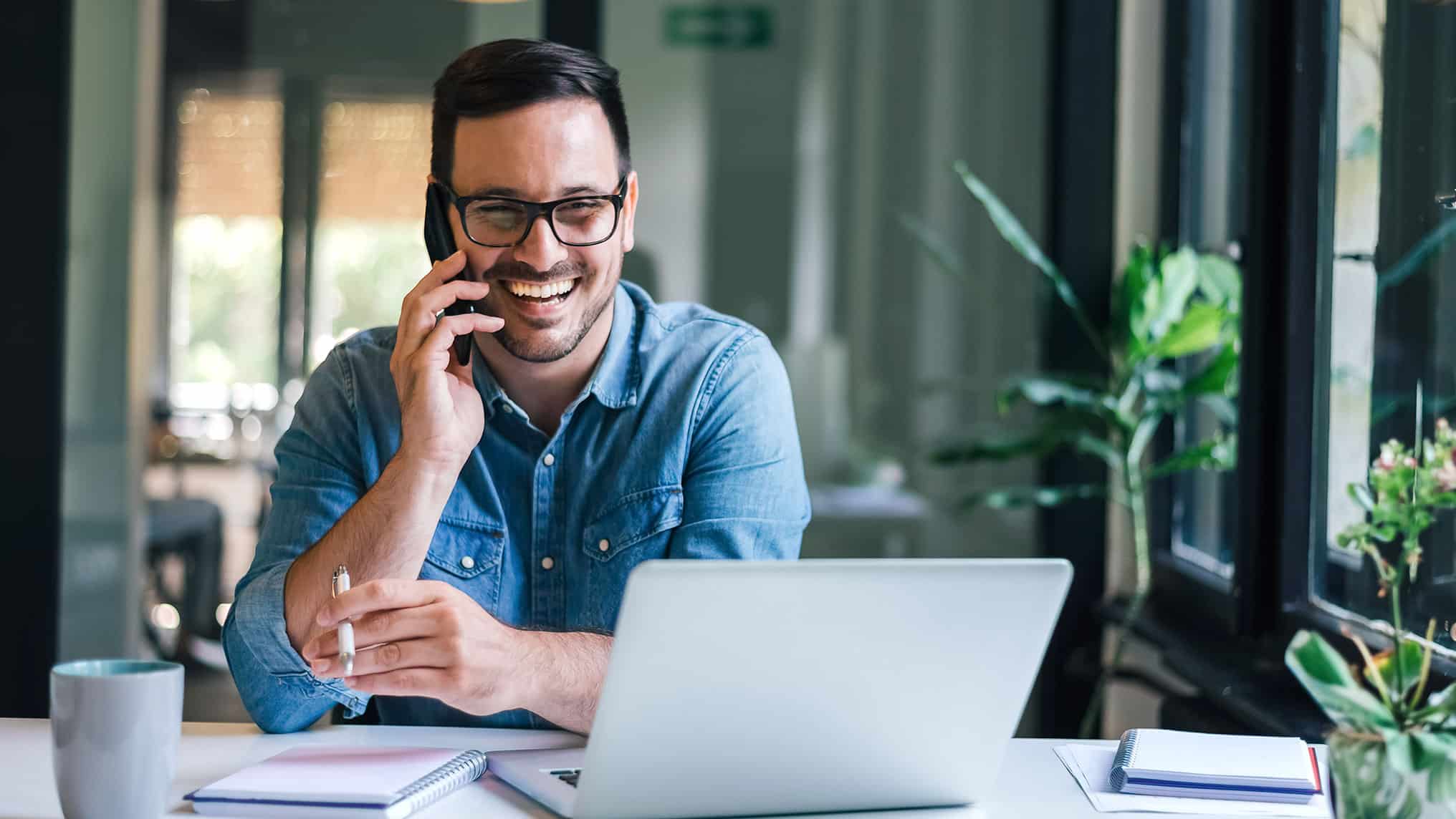 Smiling man in office working on phone and lapop