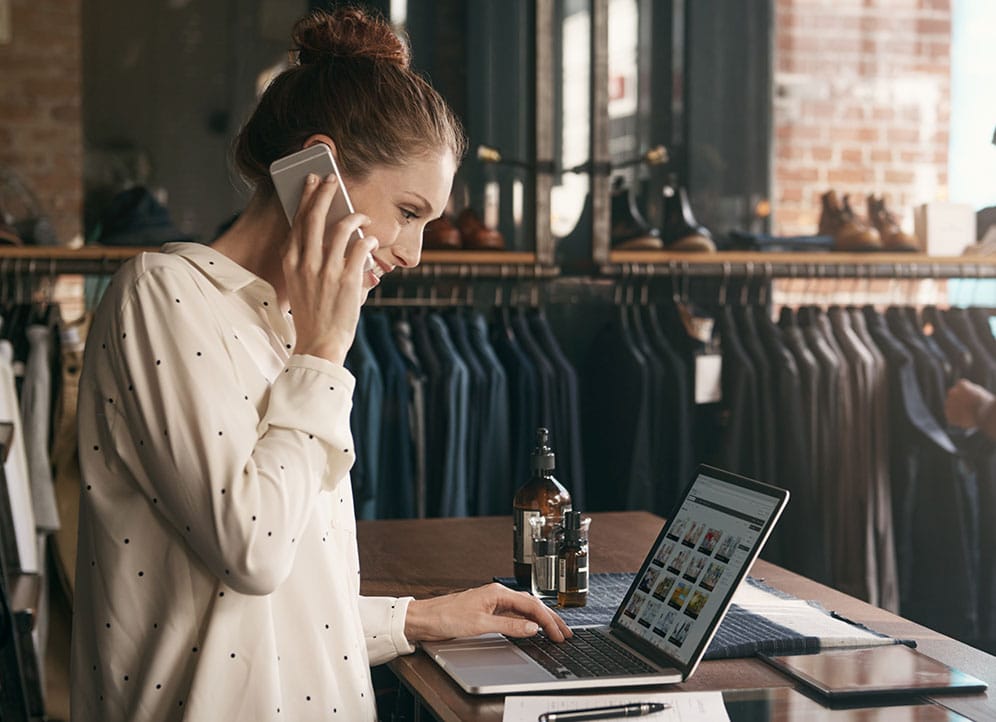 Woman talking to customer on phone and looking at laptop in retail boutique