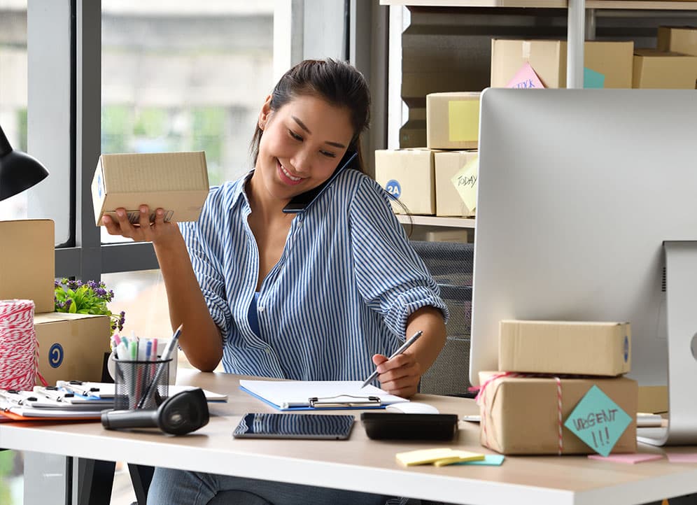 Woman holding package taking order from customer on phone in office